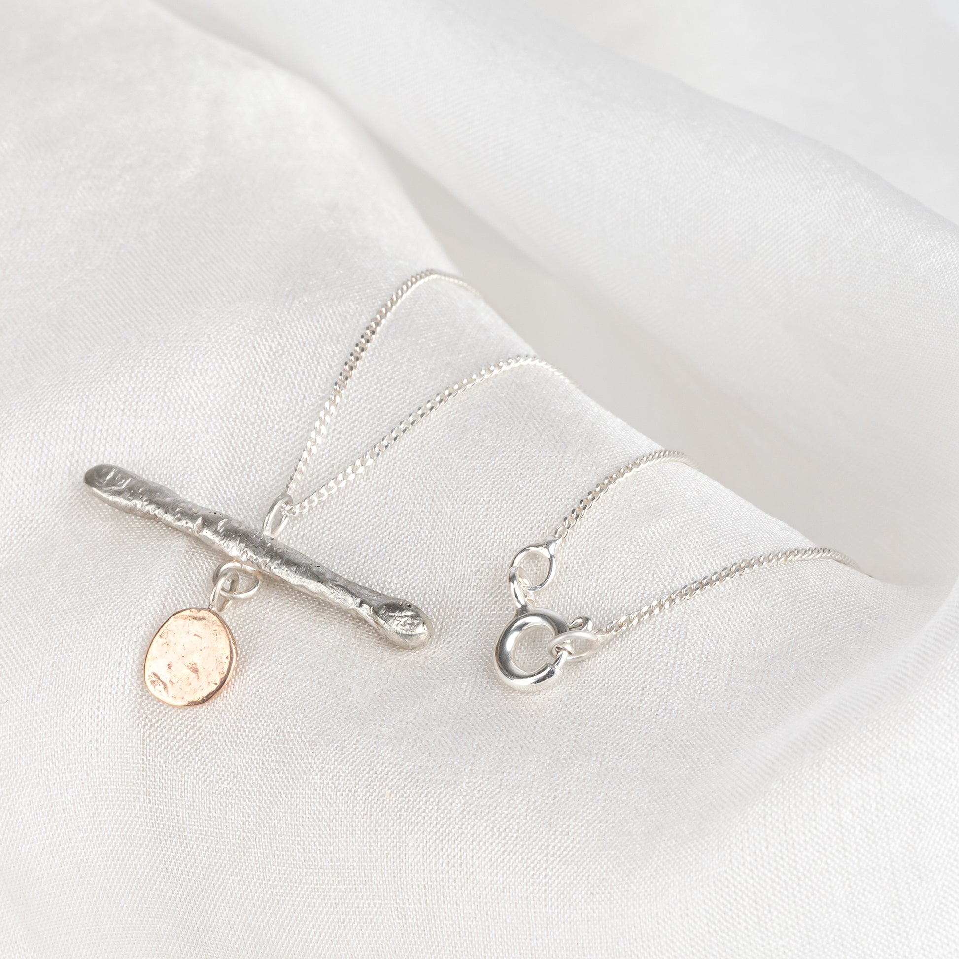 A silver bar pendant necklace with a gold drop, displayed against a light background.