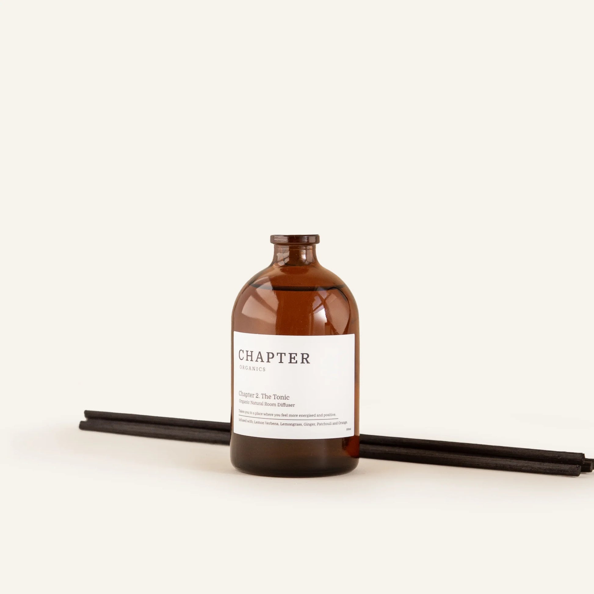 A brown glass bottle labelled "CHAPTER ORGANICS" sits on a light background. Two black incense sticks lie beside the bottle, creating a minimalist and calming aesthetic.