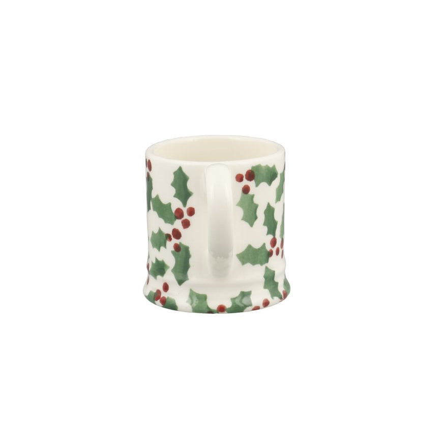 A small white ceramic mug decorated with a green holly and red berry pattern, shown against a plain white background.