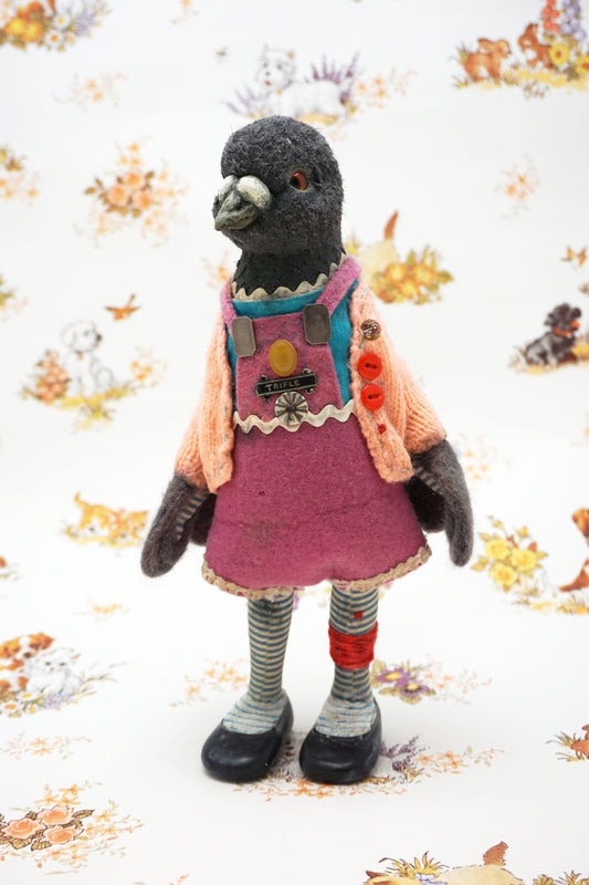 A plush pigeon dressed in a pink dress, striped leggings, and a peach cardigan with colourful buttons stands against a whimsical background featuring small animal illustrations and floral patterns.