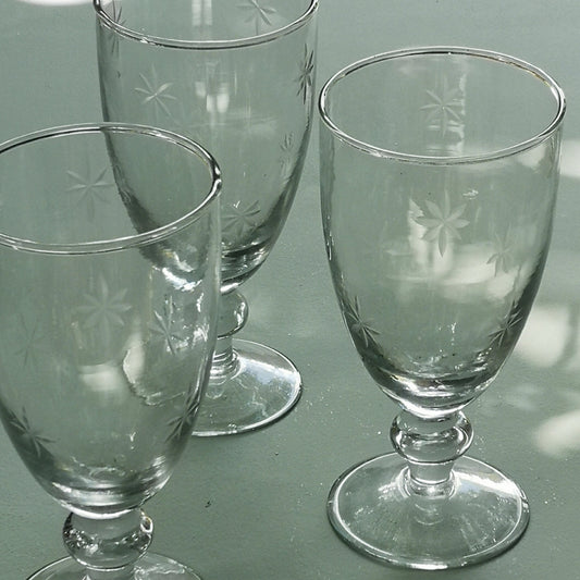 Three clear water glasses with etched star designs on a reflective surface