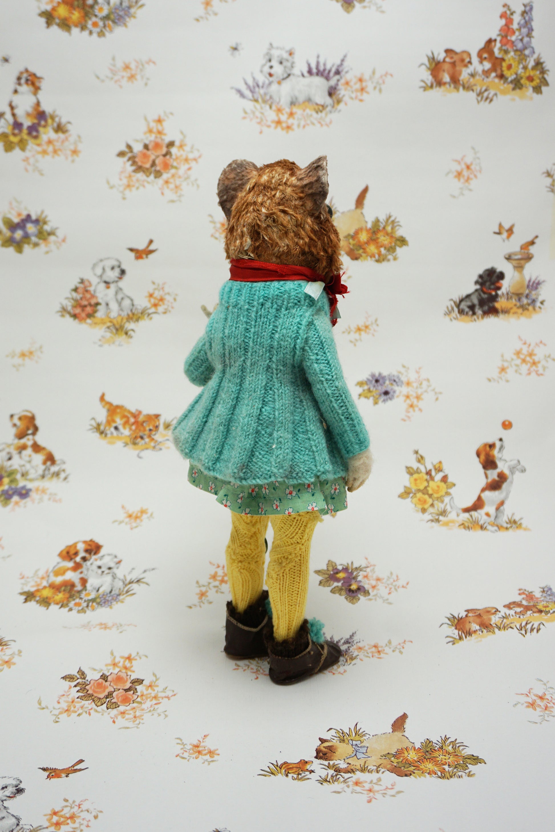 A plush guinea pig dressed in a teal cardigan, floral dress, and yellow tights holds a small stuffed animal. The background features whimsical illustrations of animals and nature scenes.