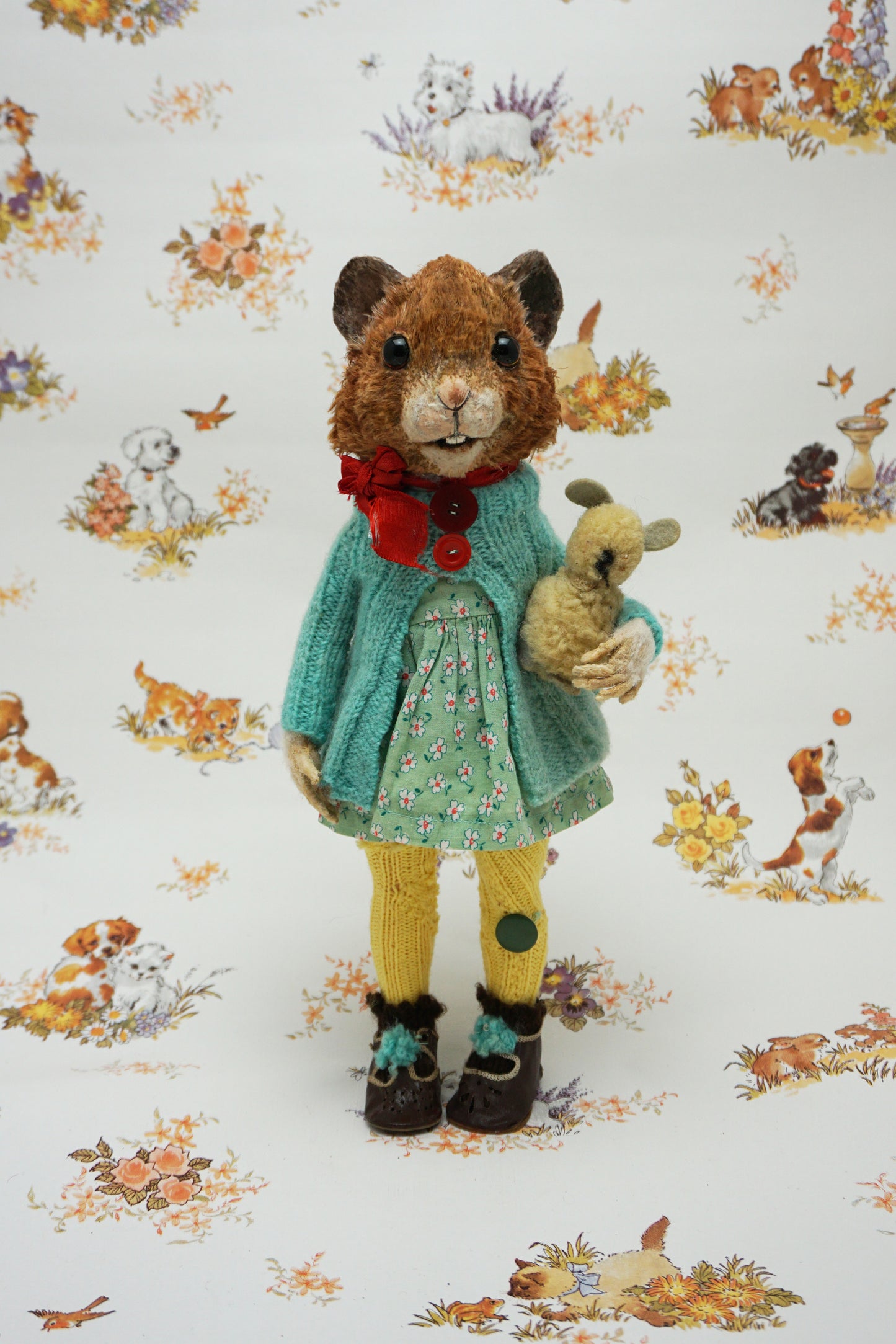 A plush guinea pig dressed in a teal cardigan, floral dress, and yellow tights holds a small stuffed animal. The background features whimsical illustrations of animals and nature scenes.