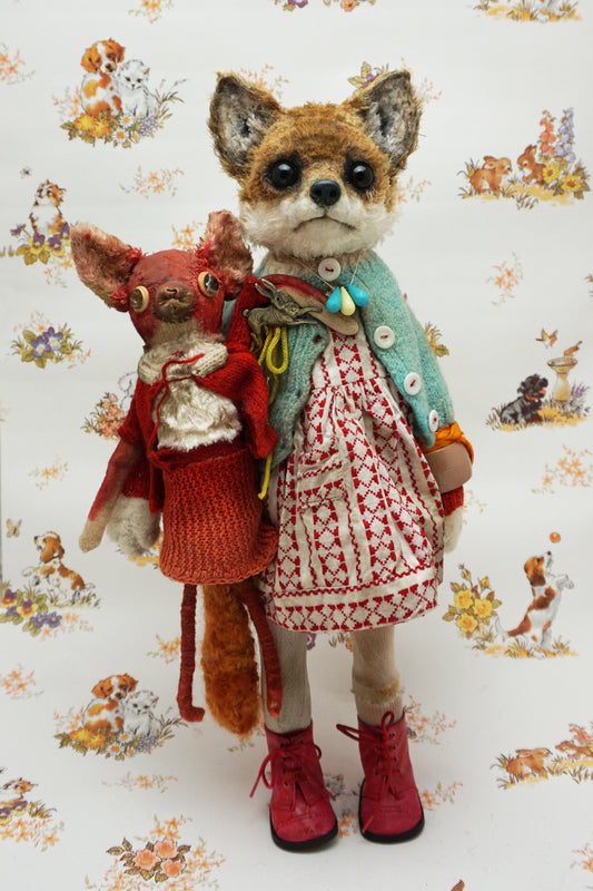 A plush fox toy dressed in a patterned red and white dress, teal cardigan, and red boots holds a smaller red plush creature. The background features a whimsical animal print with various small animals.