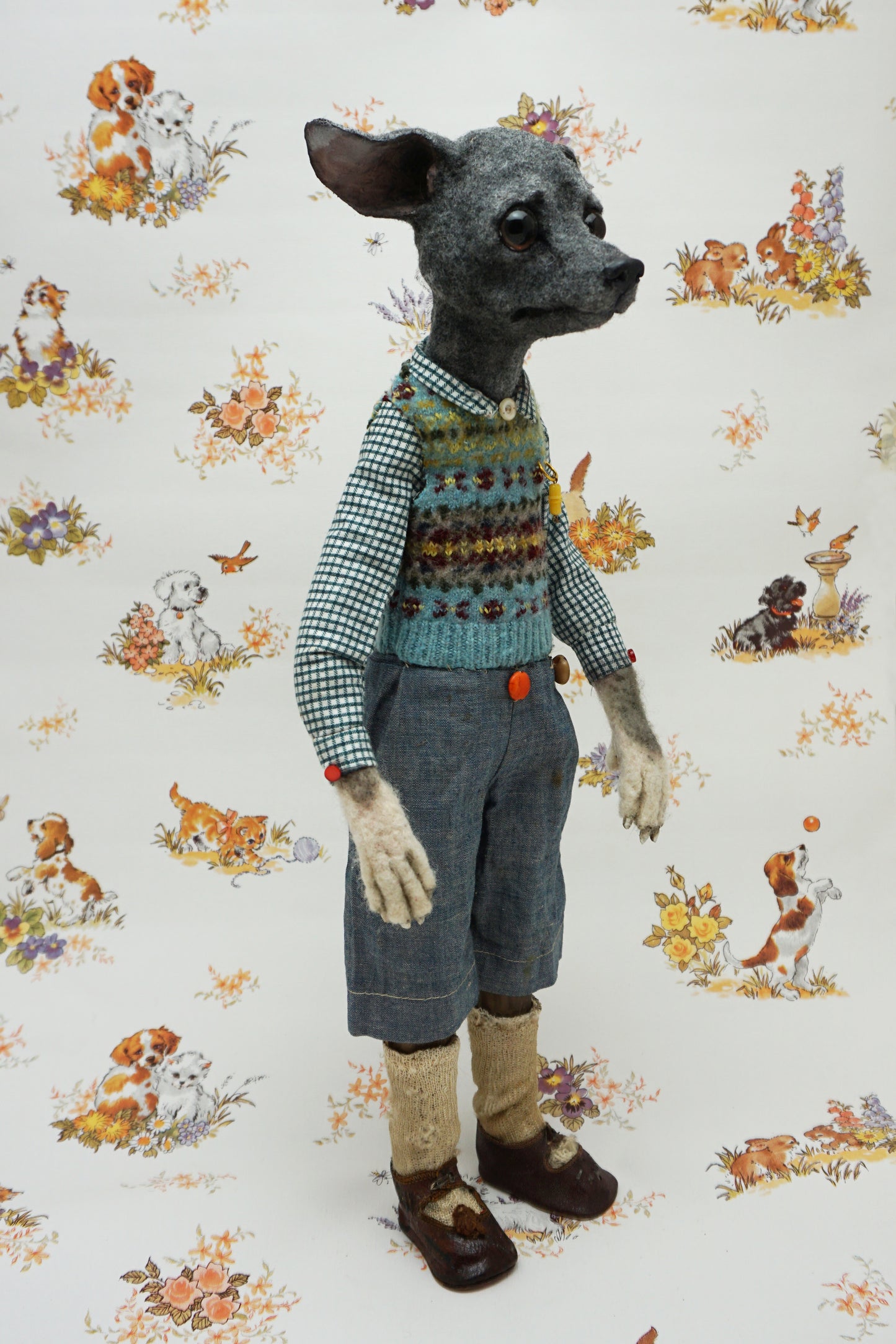 A whimsical, anthropomorphic dog figure stands upright, dressed in a checked shirt, patterned vest, and denim shorts. The background features a vintage-style wallpaper with illustrations of playful dogs and floral motifs.