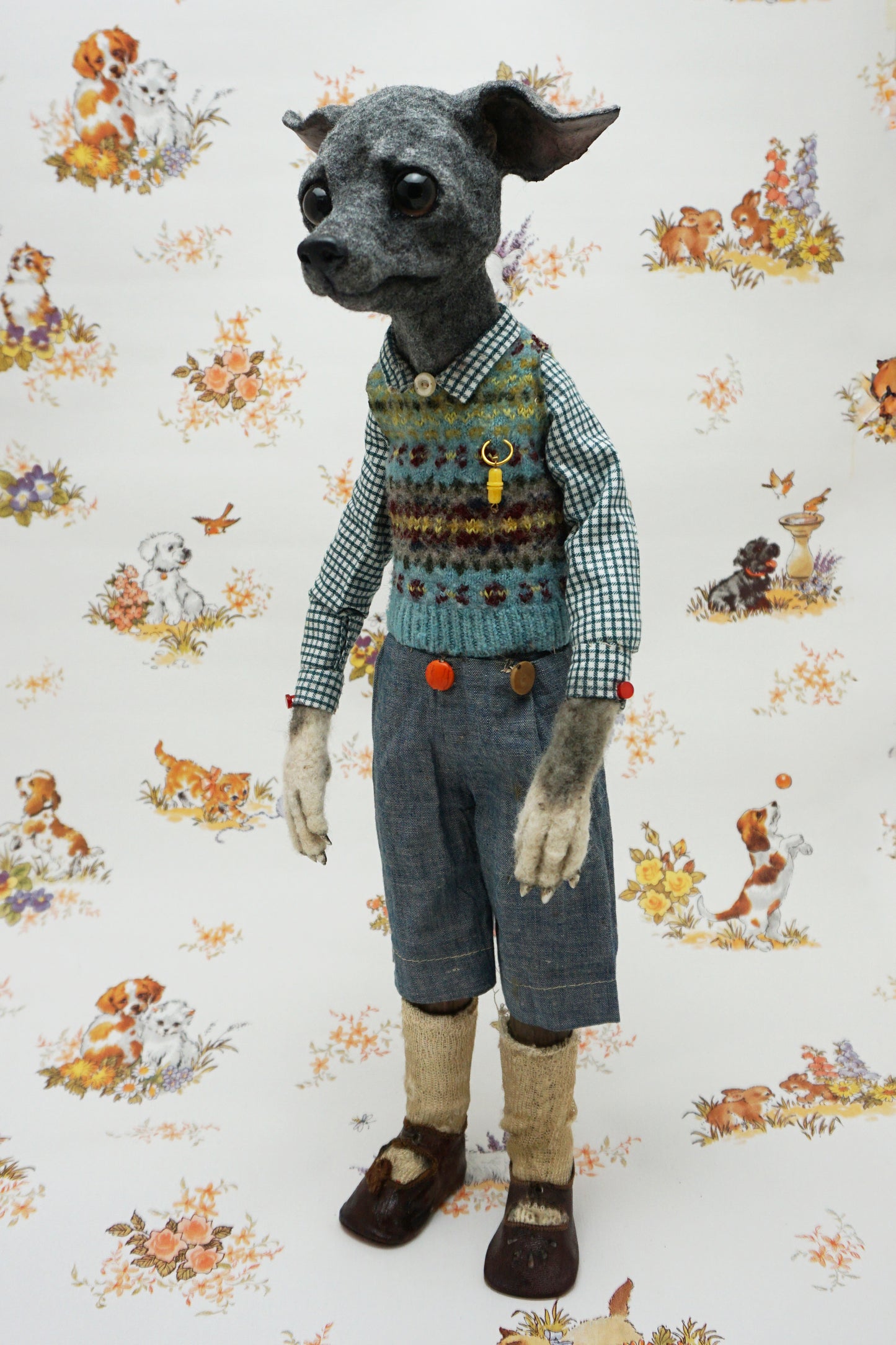 A whimsical, anthropomorphic dog figure stands upright, dressed in a checked shirt, patterned vest, and denim shorts. The background features a vintage-style wallpaper with illustrations of playful dogs and floral motifs.