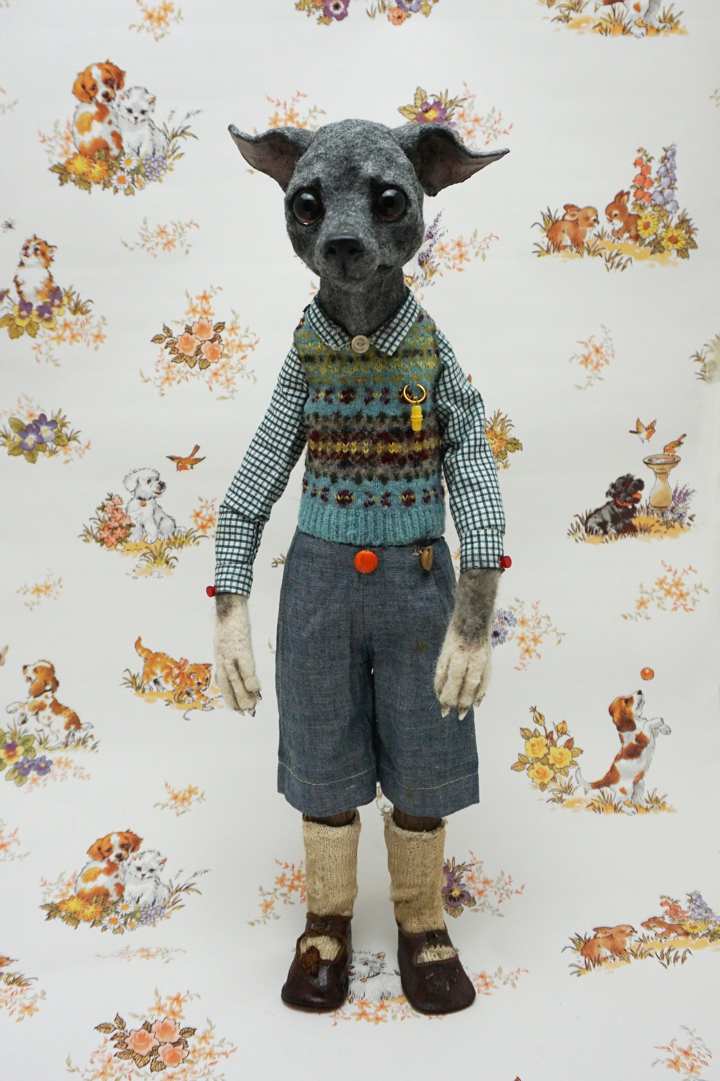 A whimsical, anthropomorphic dog figure stands upright, dressed in a checked shirt, patterned vest, and denim shorts. The background features a vintage-style wallpaper with illustrations of playful dogs and floral motifs.