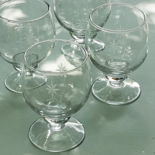 Set of four clear wine glasses with etched star patterns on a light green surface.
