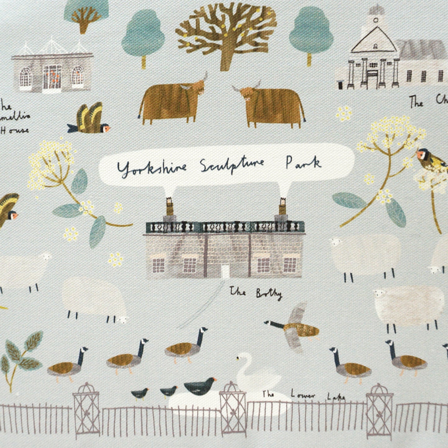 A tea cosy featuring a whimsical illustration of Yorkshire landscapes, including farms, trees, and animals like sheep and birds. The design is in soft pastel colours, with a grey trim and a tag attached, adding a charming touch to any kitchen.