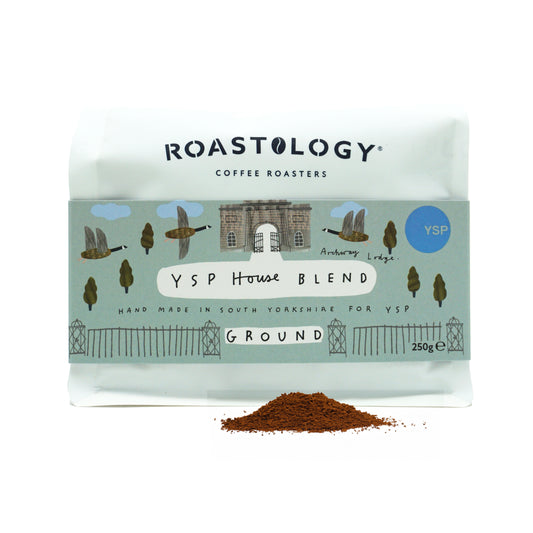 A white packet featuring a blue label with illustrations of geese and trees, with a pile of ground coffee in front.