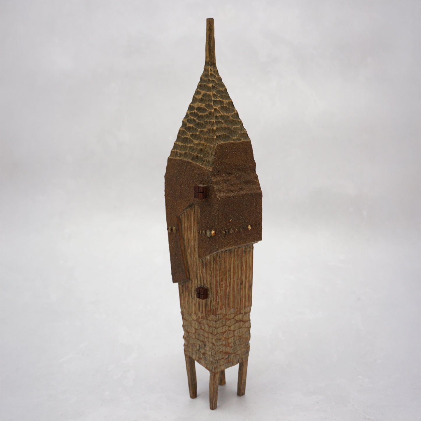 A pointy wooden house with a hand carved roof and body. The house has four legs and small wooden windows on the front.