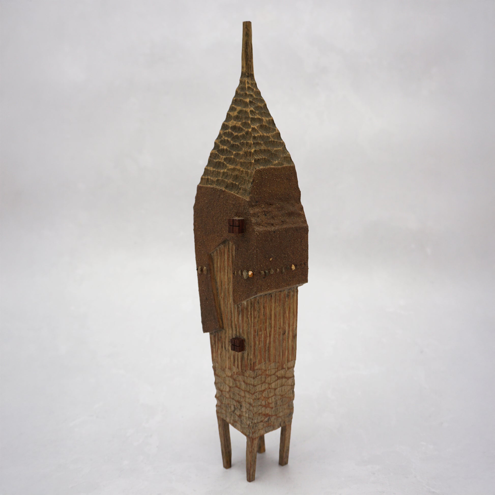 A pointy wooden house with a hand carved roof and body. The house has four legs and small wooden windows on the front.