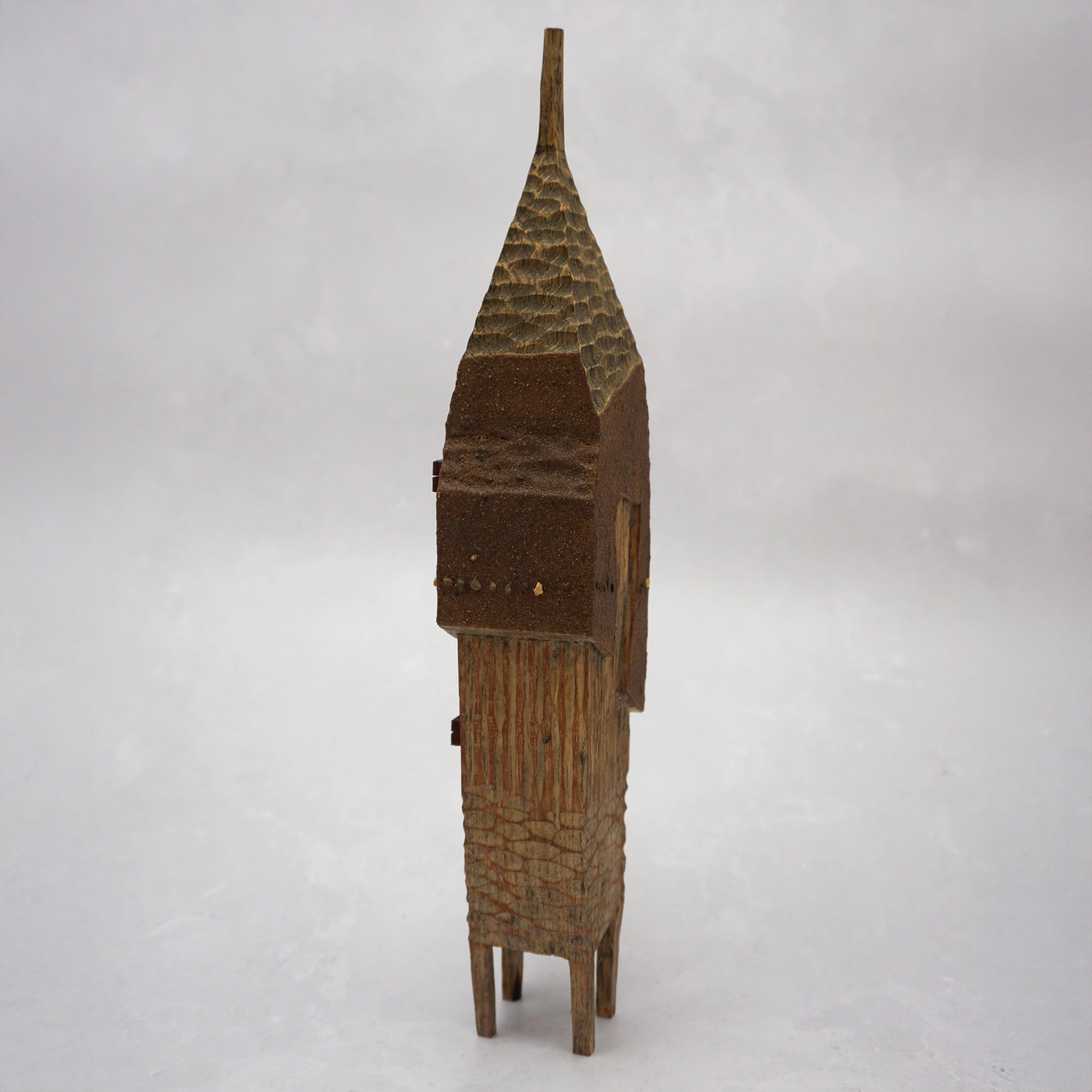 A pointy wooden house with a hand carved roof and body. The house has four legs and small wooden windows on the front.