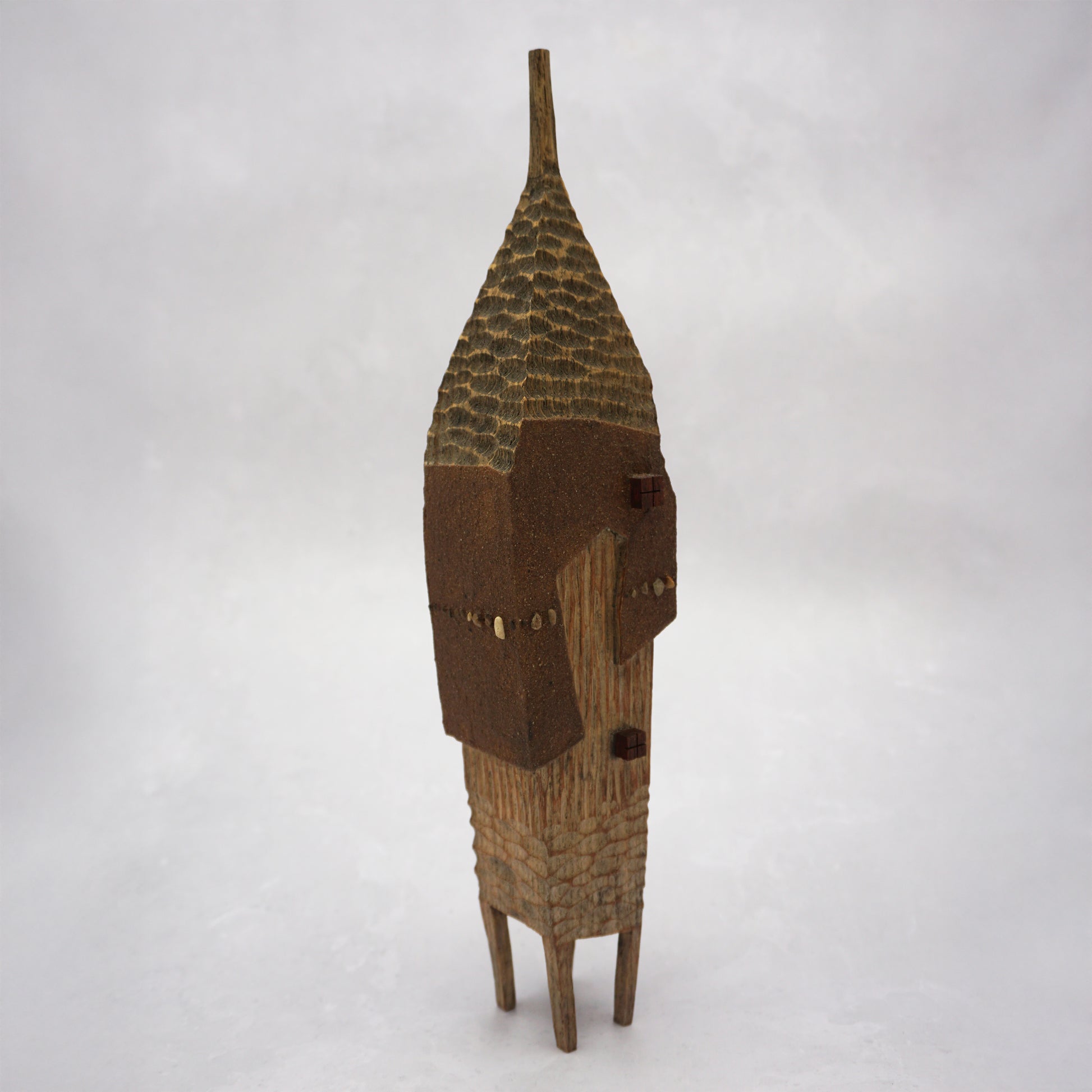 A pointy wooden house with a hand carved roof and body. The house has four legs and small wooden windows on the front.