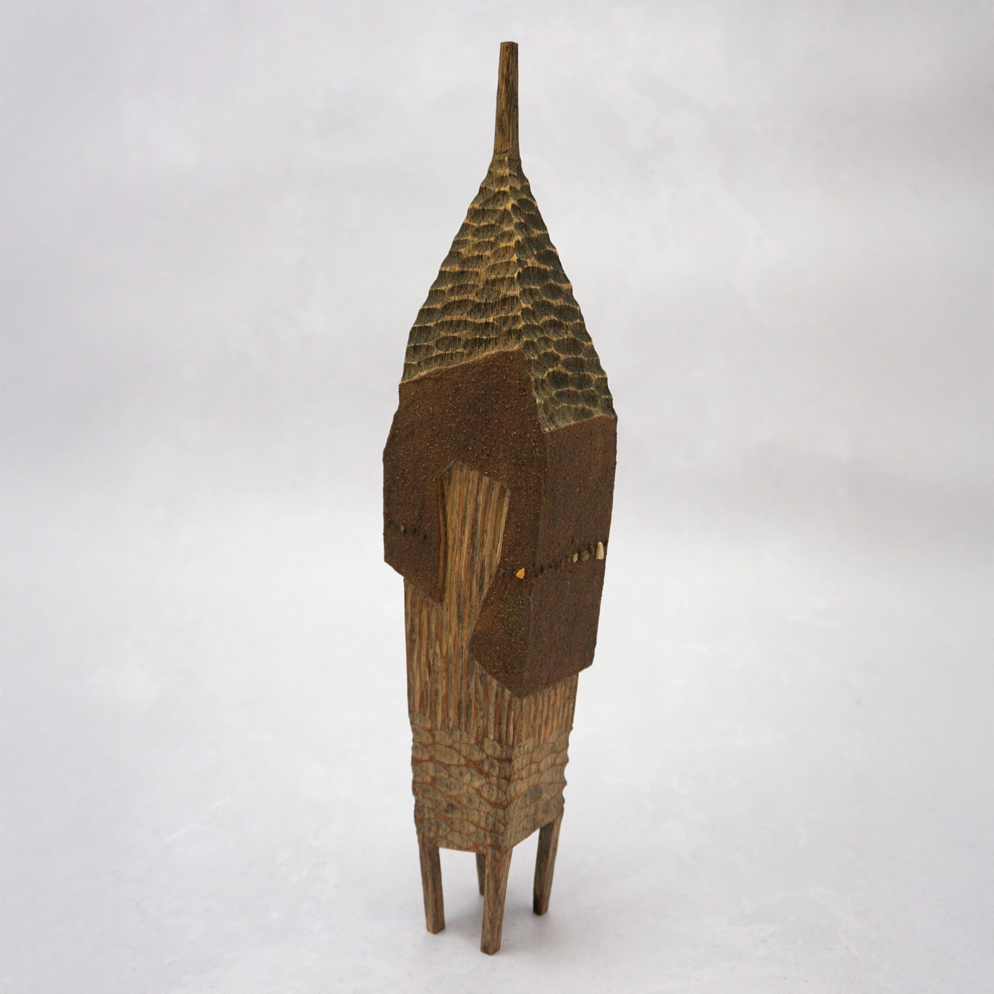 A pointy wooden house with a hand carved roof and body. The house has four legs and small wooden windows on the front.