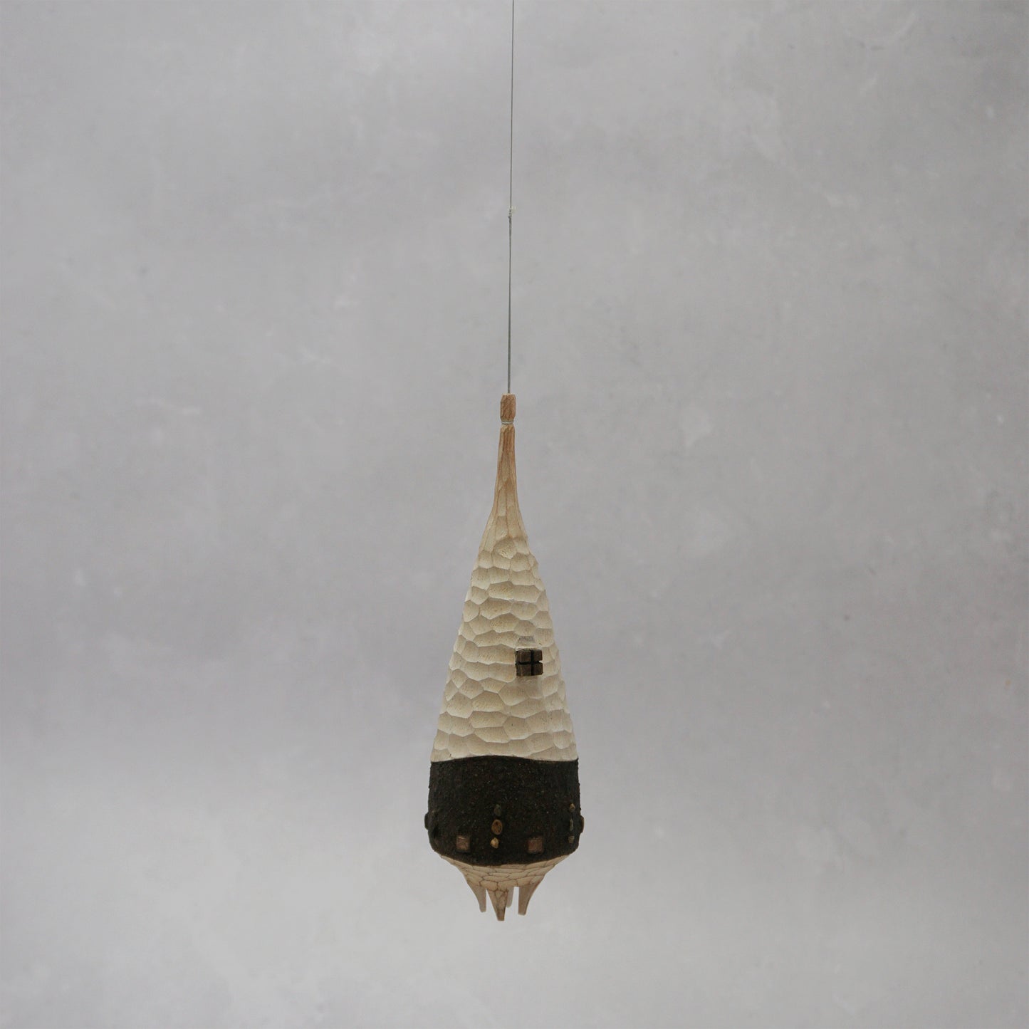 Decorative hanging wooden house with textured design on a plain background. The house has four legs and wooden windows, and is shaped almost like a beehive. 