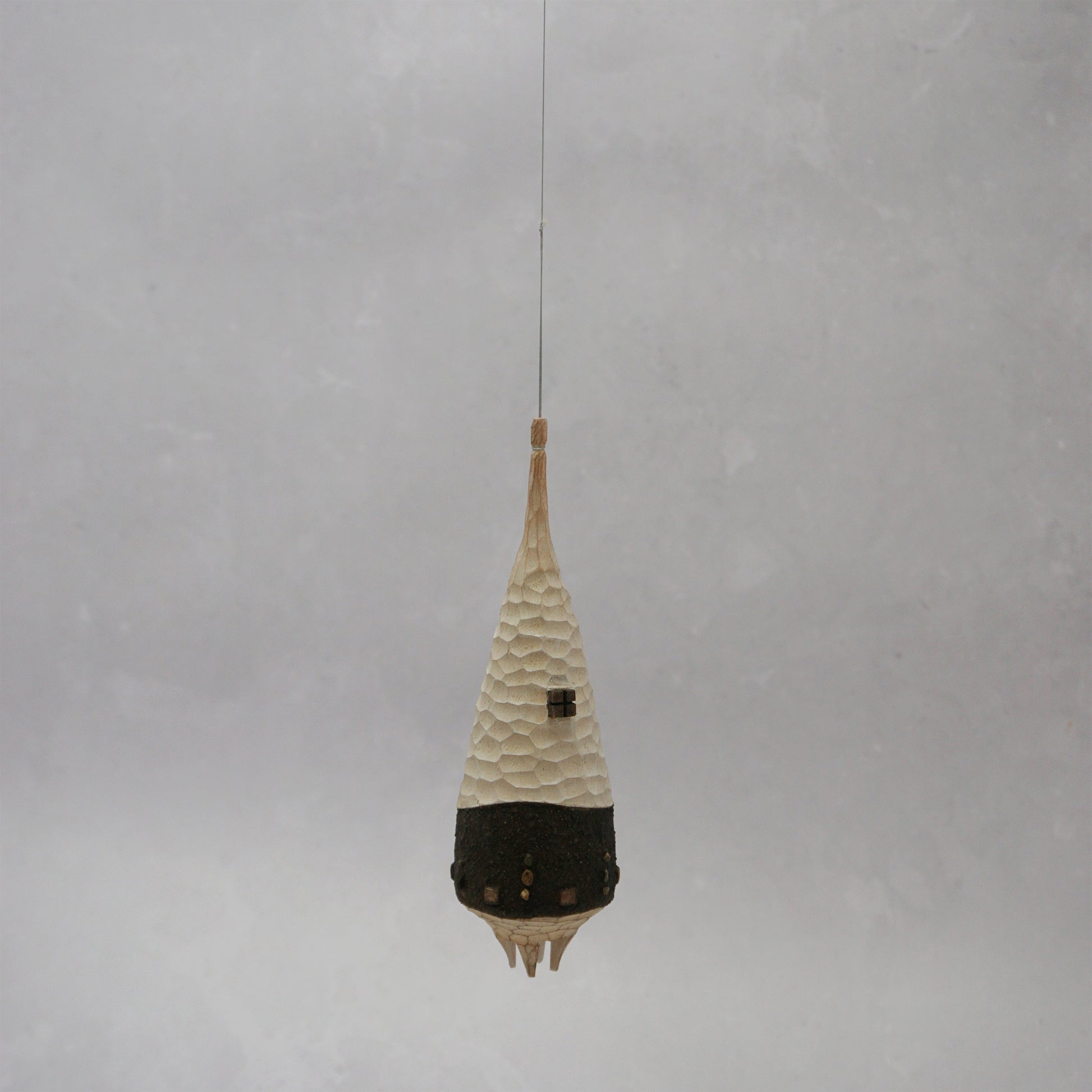 Decorative hanging wooden house with textured design on a plain background. The house has four legs and wooden windows, and is shaped almost like a beehive. 