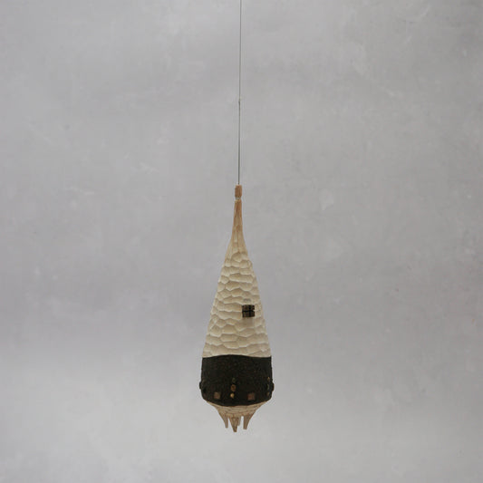 Decorative hanging wooden house with textured design on a plain background. The house has four legs and wooden windows, and is shaped almost like a beehive. 