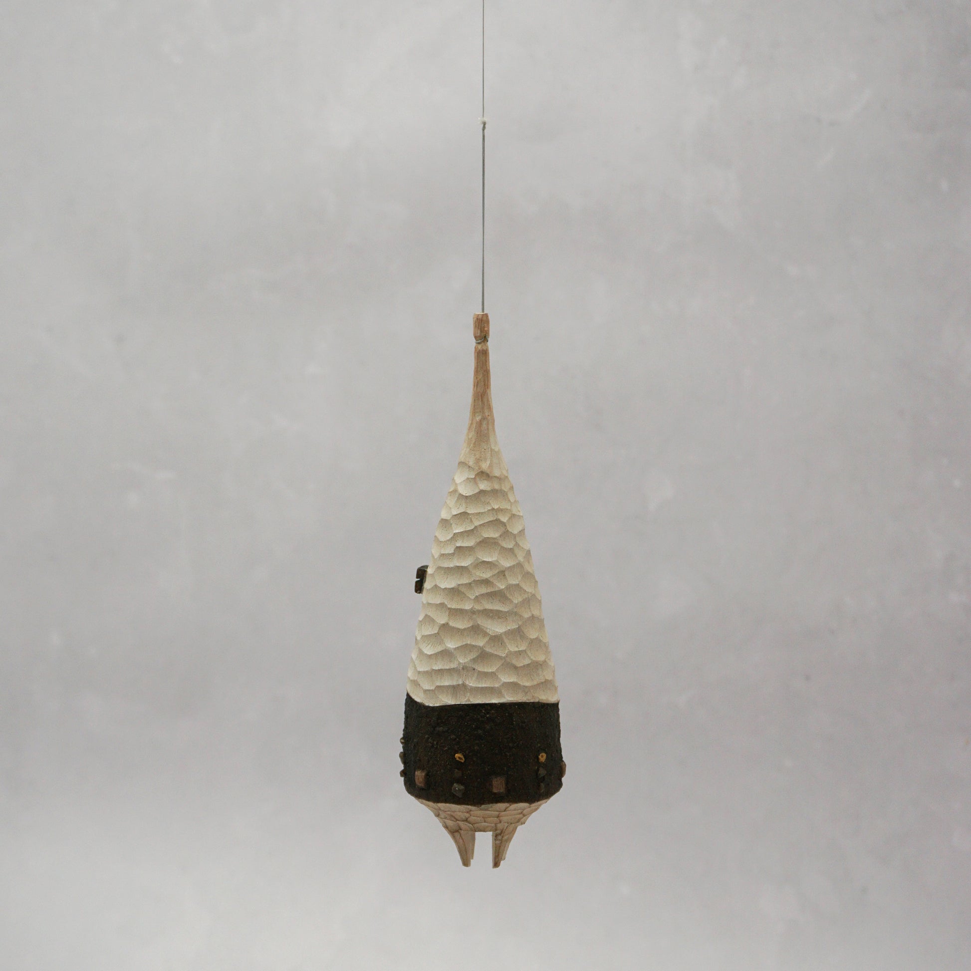 Decorative hanging wooden house with textured design on a plain background. The house has four legs and wooden windows, and is shaped almost like a beehive. 