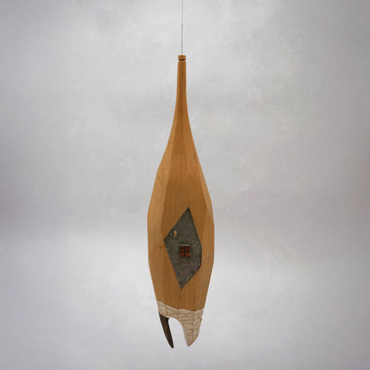 Decorative hand carved wooden house shaped like a small tower on a plain background. The house has legs, windows and a thin chimney which thread is coming out of to hang the house. The house looks to be made from an oak coloured wood.