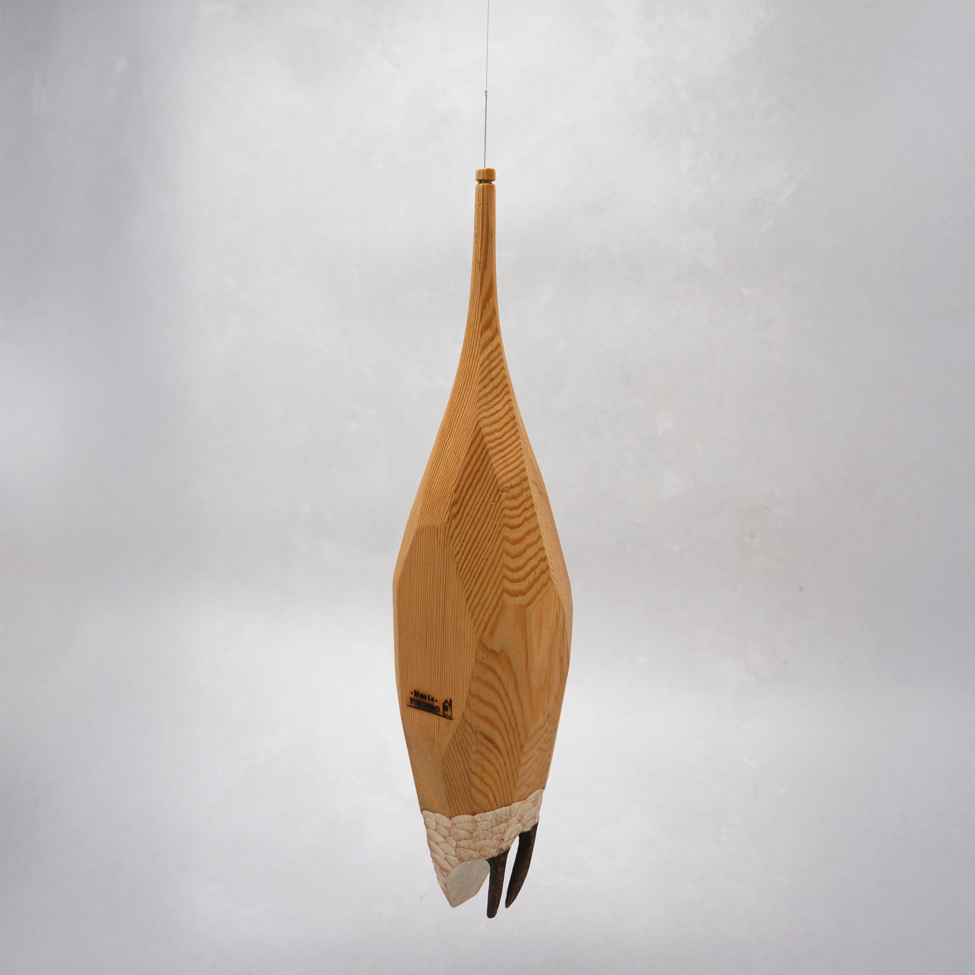 Decorative hand carved wooden house shaped like a small tower on a plain background. The house has legs, windows and a thin chimney which thread is coming out of to hang the house. The house looks to be made from an oak coloured wood.