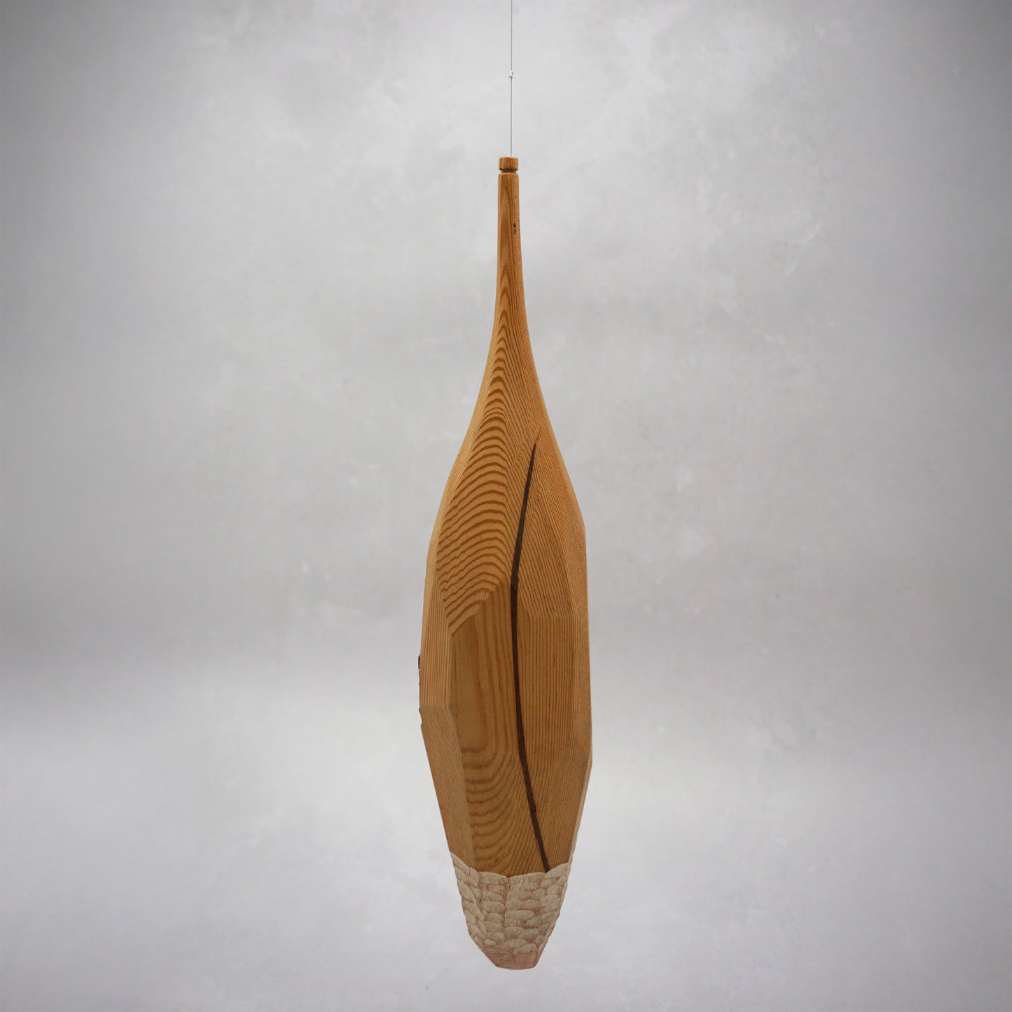 Decorative hand carved wooden house shaped like a small tower on a plain background. The house has legs, windows and a thin chimney which thread is coming out of to hang the house. The house looks to be made from an oak coloured wood.