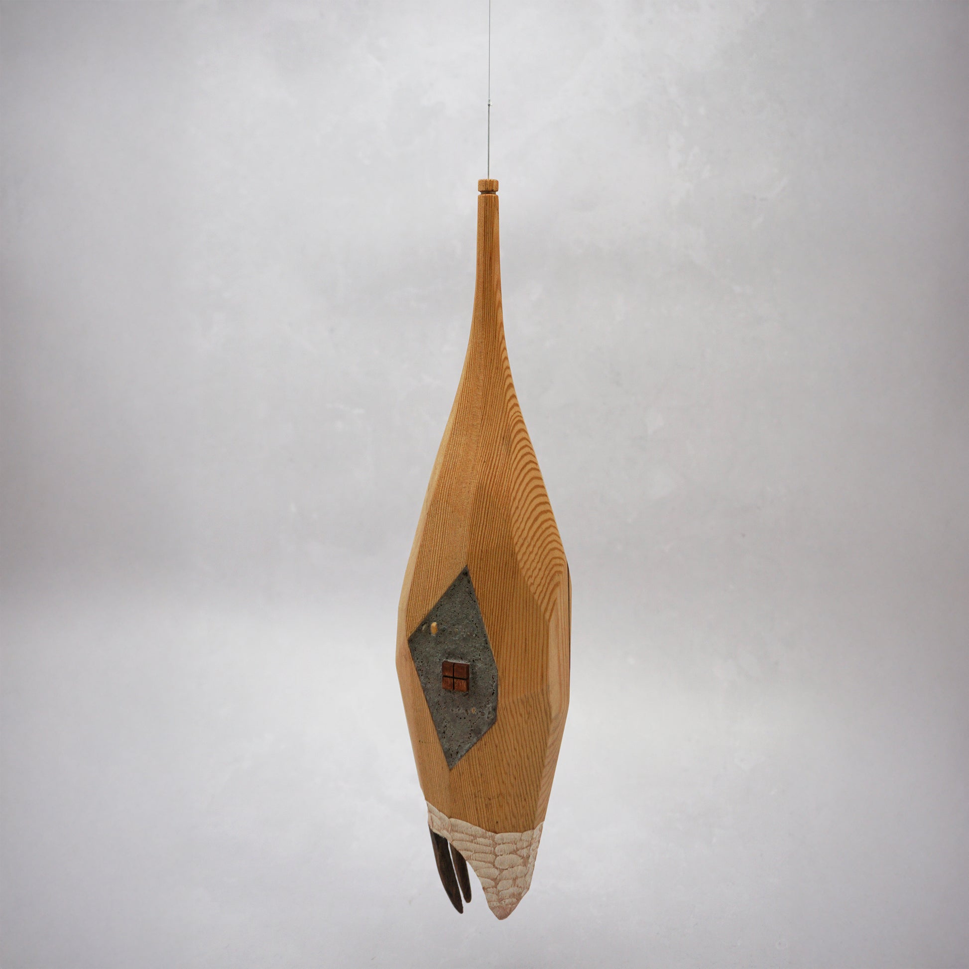 Decorative hand carved wooden house shaped like a small tower on a plain background. The house has legs, windows and a thin chimney which thread is coming out of to hang the house. The house looks to be made from an oak coloured wood.