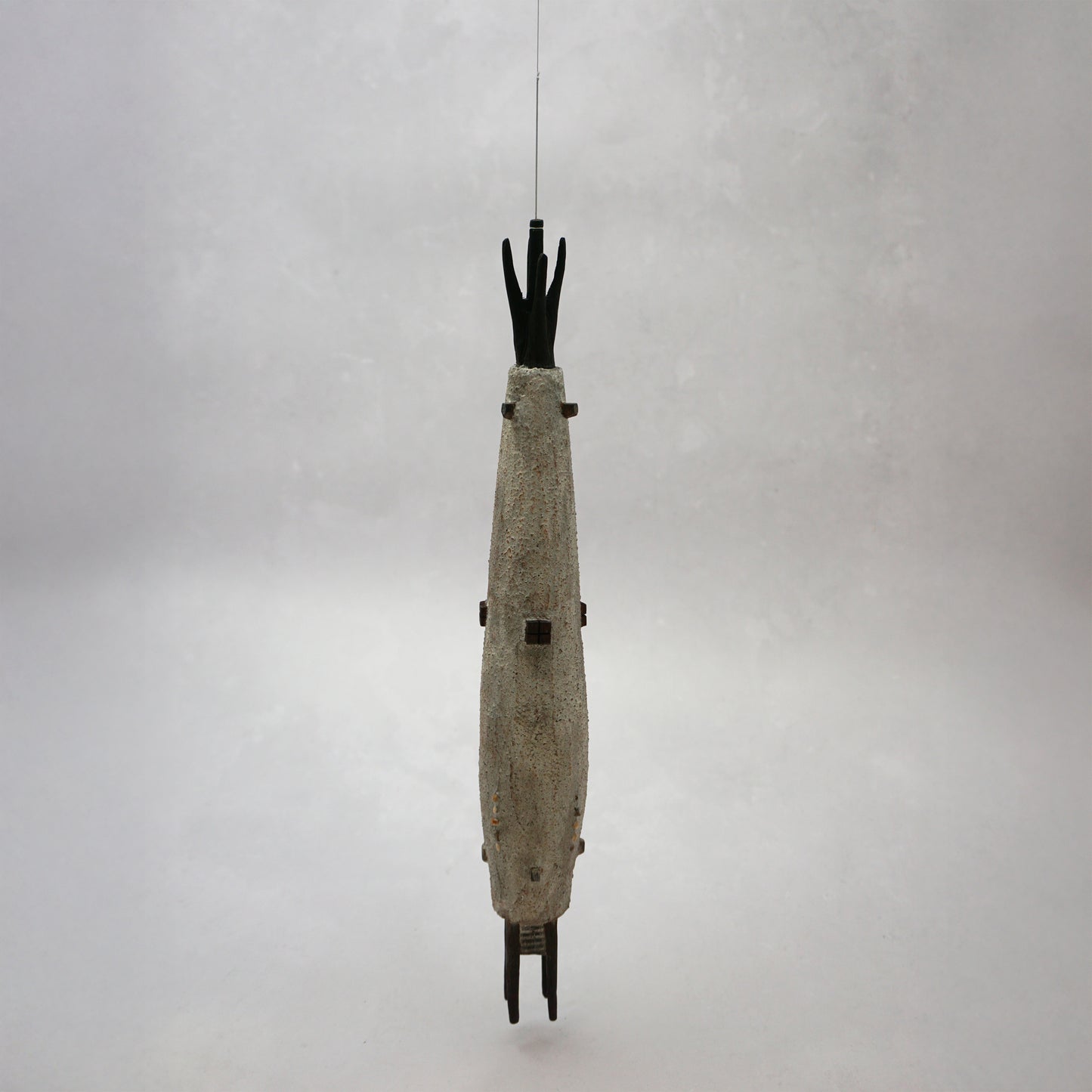 Hanging wooden house in a long slender shape with four legs at the bottom. The house is grey with dark brown windows and turrets and it has grey thread from the top which is hanging the piece