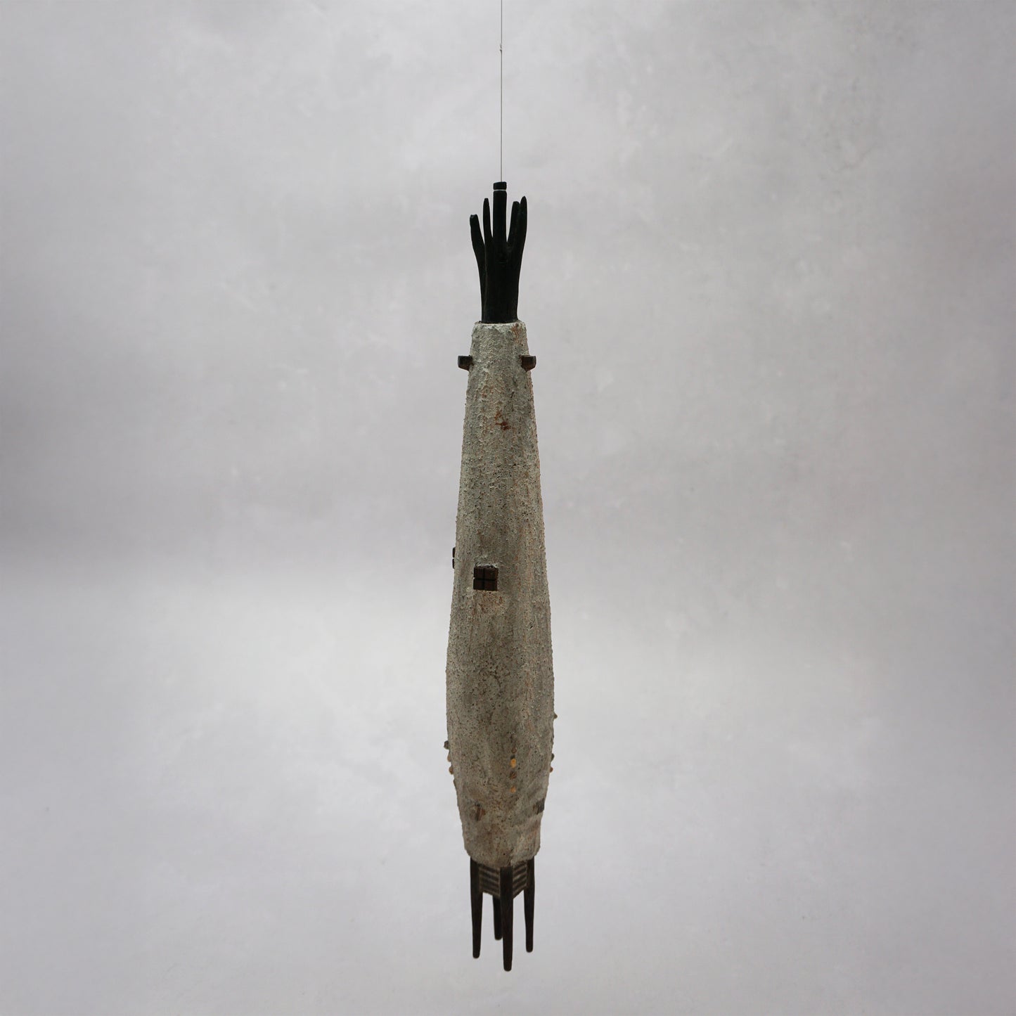 Hanging wooden house in a long slender shape with four legs at the bottom. The house is grey with dark brown windows and turrets and it has grey thread from the top which is hanging the piece