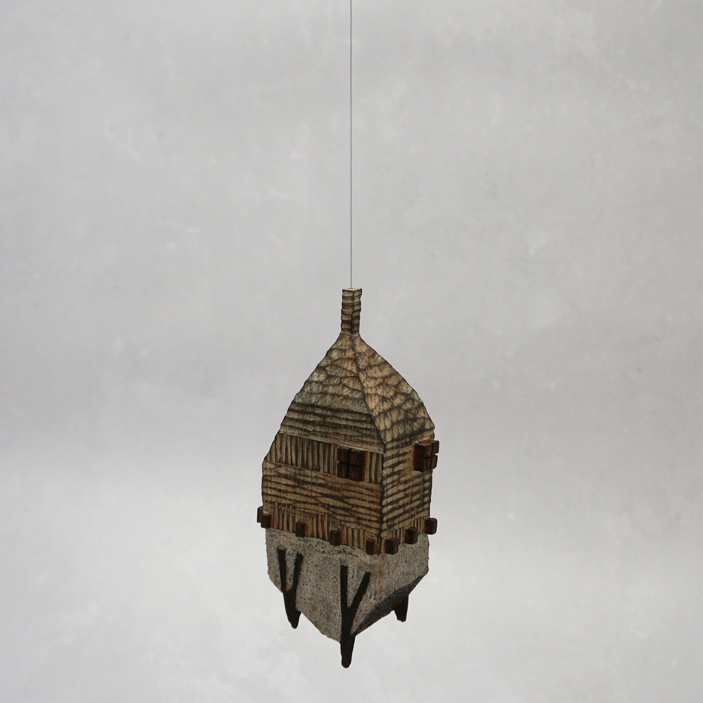 Decorative hand carved wooden house shaped like a small tower on a plain background. The house has legs, windows and a thin chimney which thread is coming out of t hang the house.