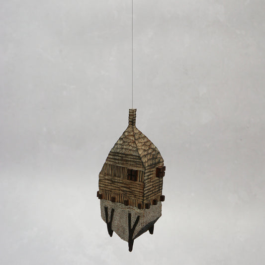 Decorative hand carved wooden house shaped like a small tower on a plain background. The house has legs, windows and a thin chimney which thread is coming out of t hang the house.
