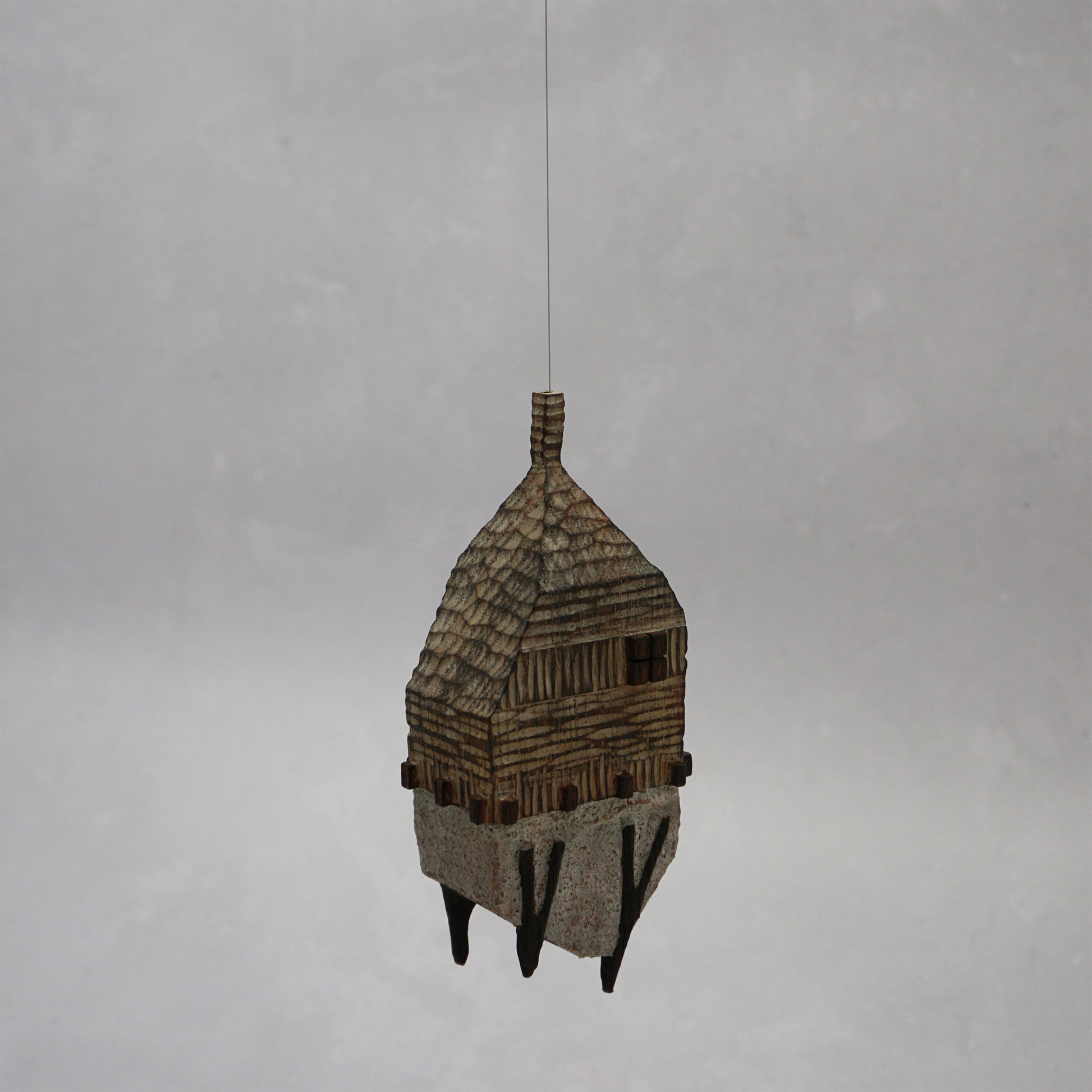 Decorative hand carved wooden house shaped like a small tower on a plain background. The house has legs, windows and a thin chimney which thread is coming out of t hang the house.