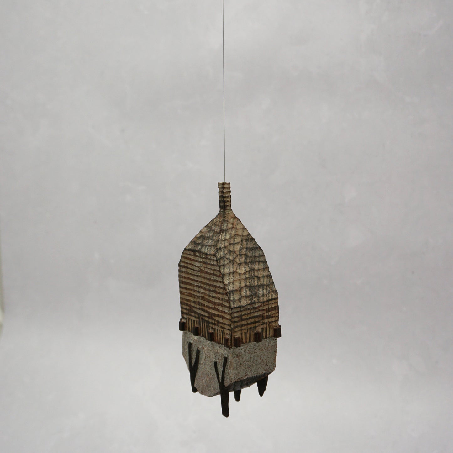 Decorative hand carved wooden house shaped like a small tower on a plain background. The house has legs, windows and a thin chimney which thread is coming out of t hang the house.