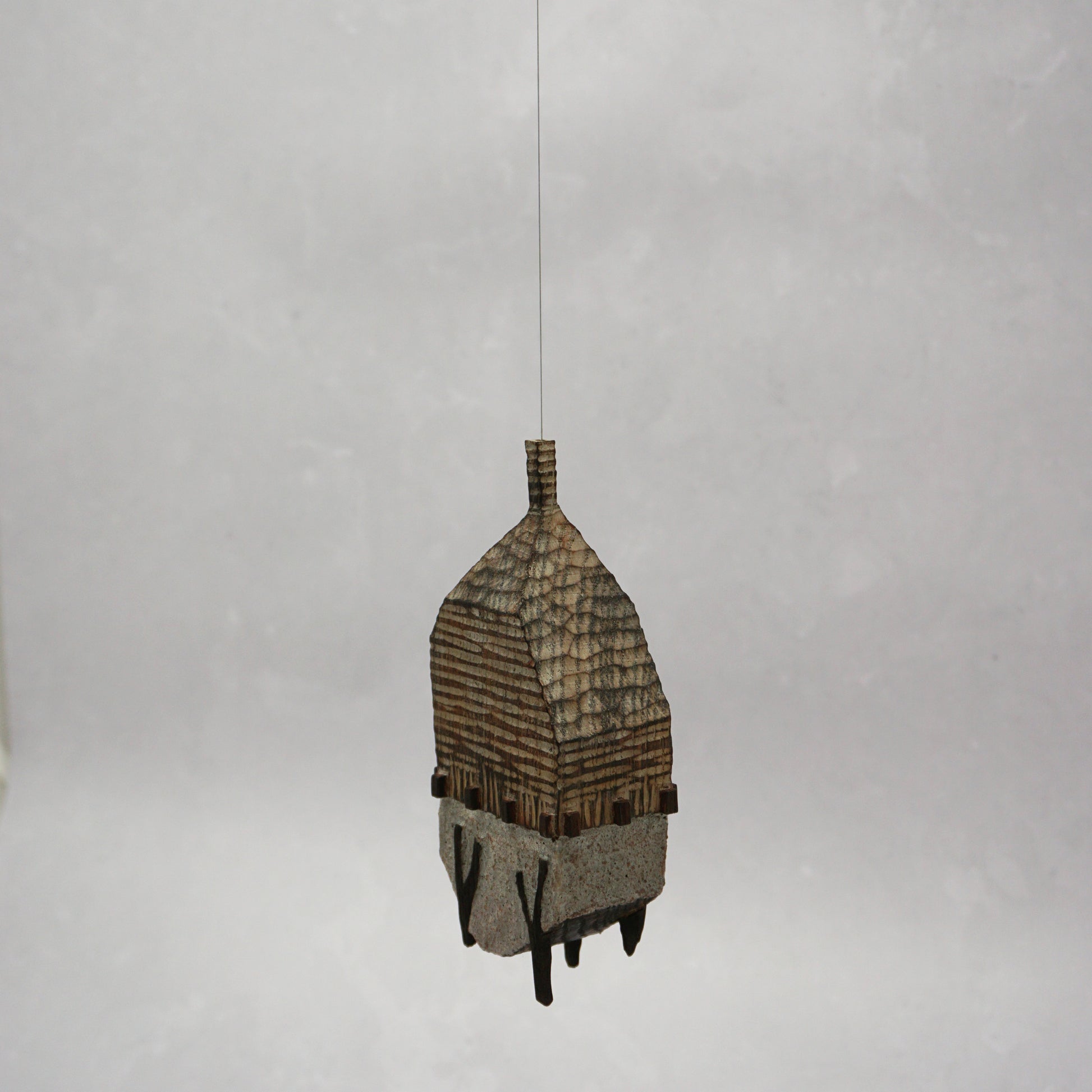 Decorative hand carved wooden house shaped like a small tower on a plain background. The house has legs, windows and a thin chimney which thread is coming out of t hang the house.