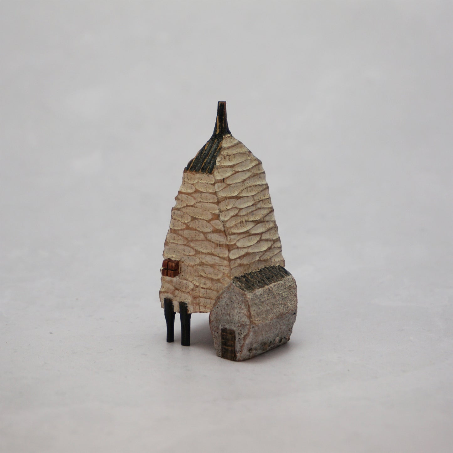 A small hand carved wooden house with a carved textured body, a small chimney and legs at the bottom.