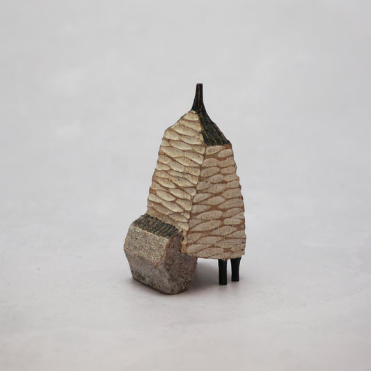 A small hand carved wooden house with a carved textured body, a small chimney and legs at the bottom.
