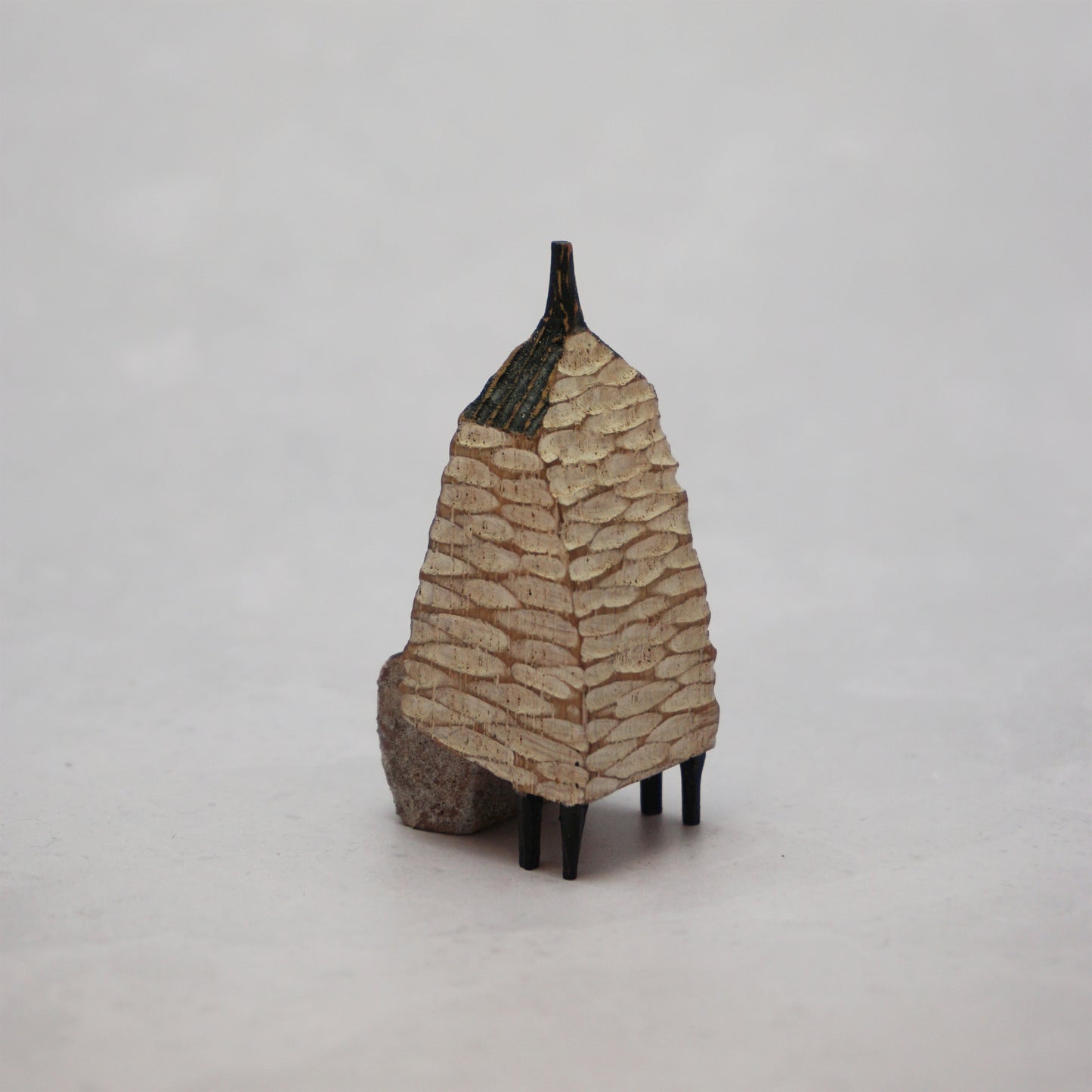 A small hand carved wooden house with a carved textured body, a small chimney and legs at the bottom.