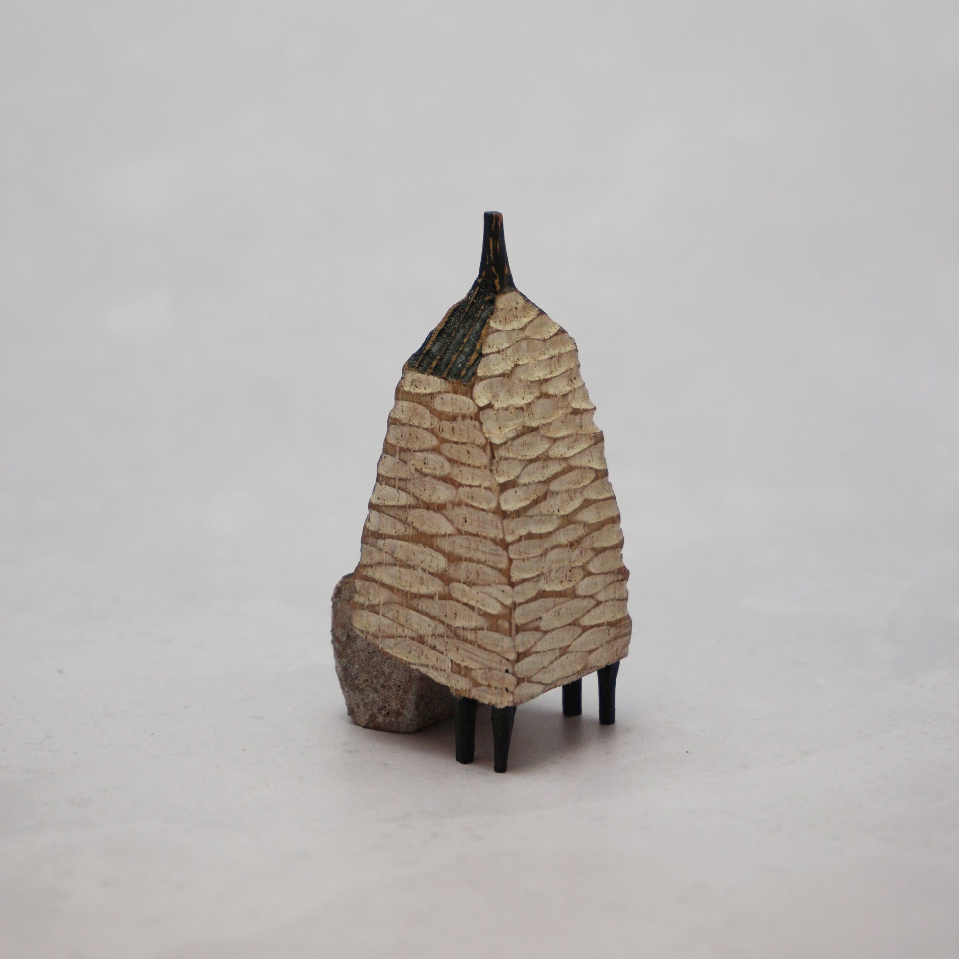 A small hand carved wooden house with a carved textured body, a small chimney and legs at the bottom.