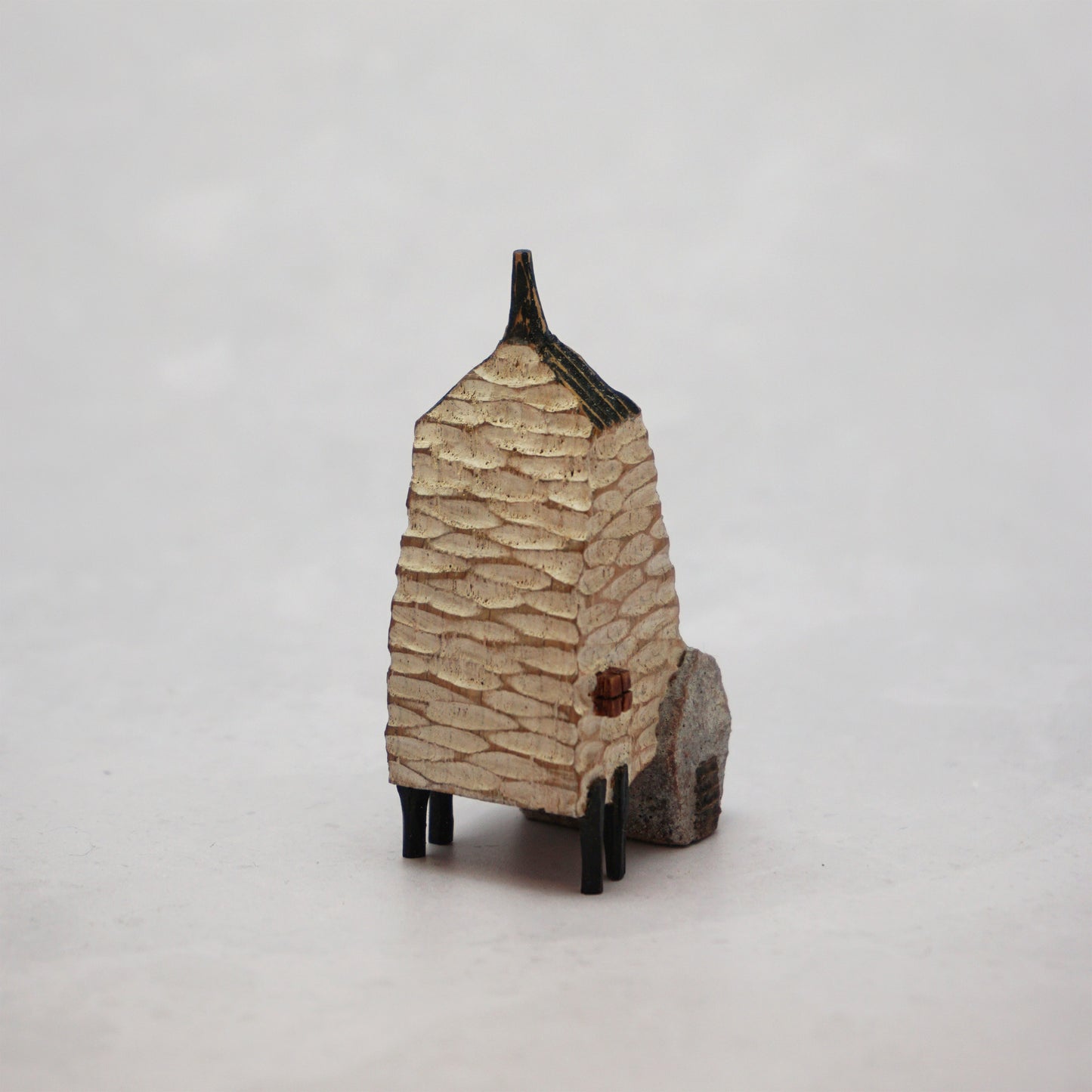 A small hand carved wooden house with a carved textured body, a small chimney and legs at the bottom.