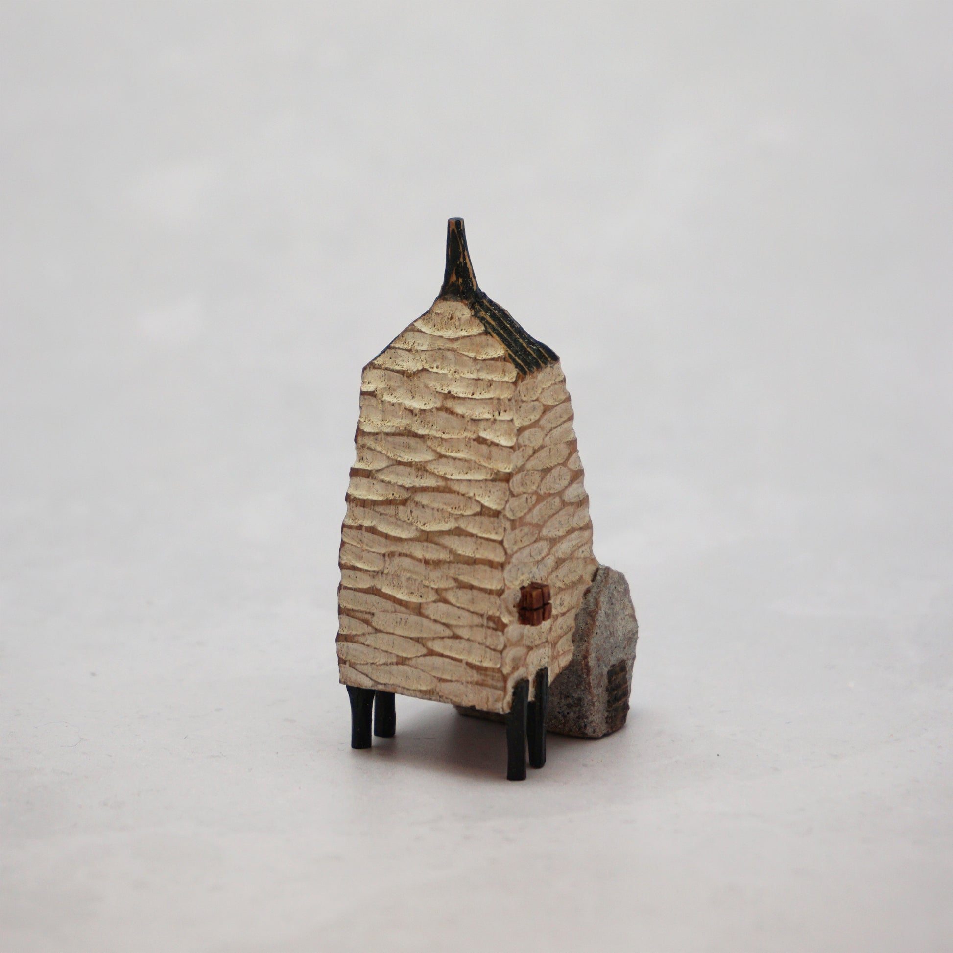 A small hand carved wooden house with a carved textured body, a small chimney and legs at the bottom.