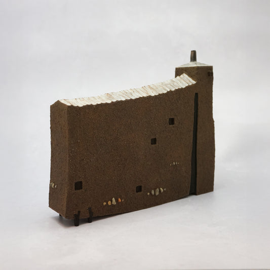 Thin, wide brown wooden house with windows and a carved, textured roof with a small chimney.