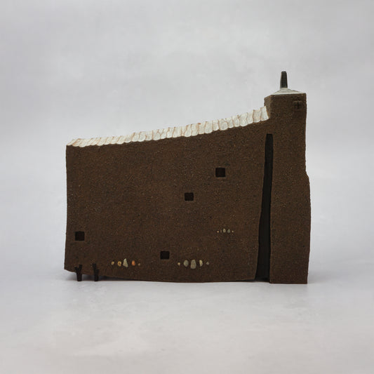 Thin, wide brown wooden house with windows and a carved, textured roof with a small chimney.