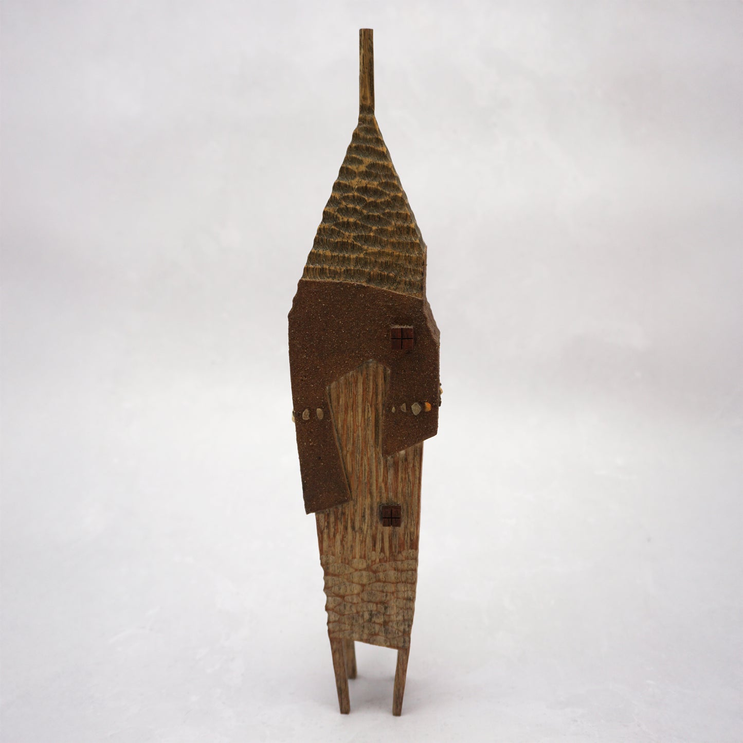 A pointy wooden house with a hand carved roof and body. The house has four legs and small wooden windows on the front.