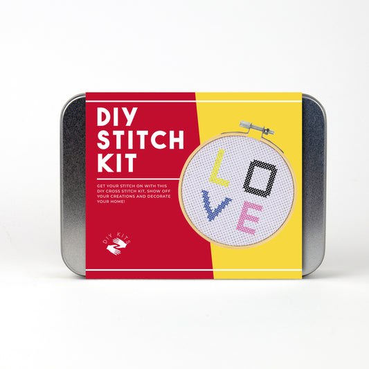 A metal tin DIY stitch kit with red and yellow branding and a picture of cross stitch on a hoop.
