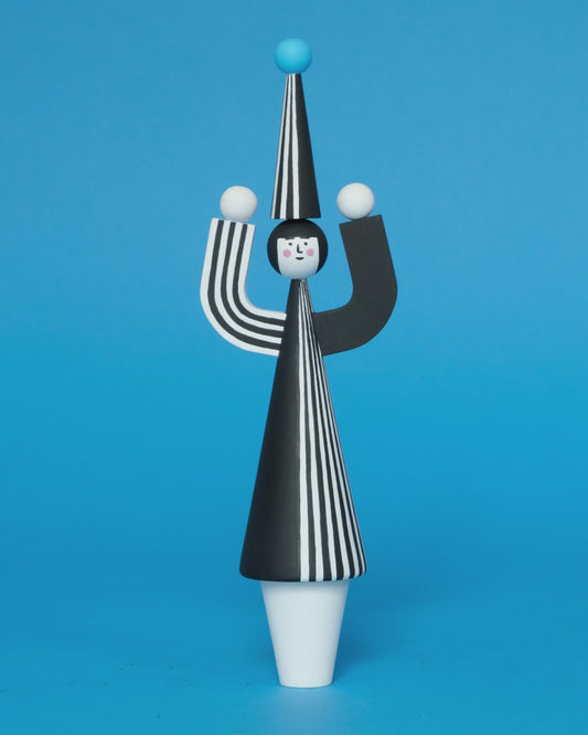 A spinning video of a wooden sculpture with a black and white stripey body with a matching headdress featuring a blue pompom on the top with white legs on a plain blue background.