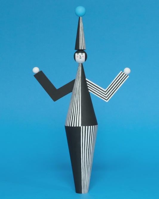 A spinning video of a wooden sculpture with a black and white stripey body with a matching headdress featuring a blue pompom on the top with white and black stripey legs on a plain blue background.