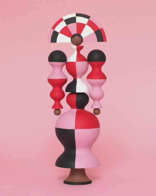 A spinning video of a colourful sculpture with a white, red, black and pink stripey curved body with a matching headdress on a plain pink background.