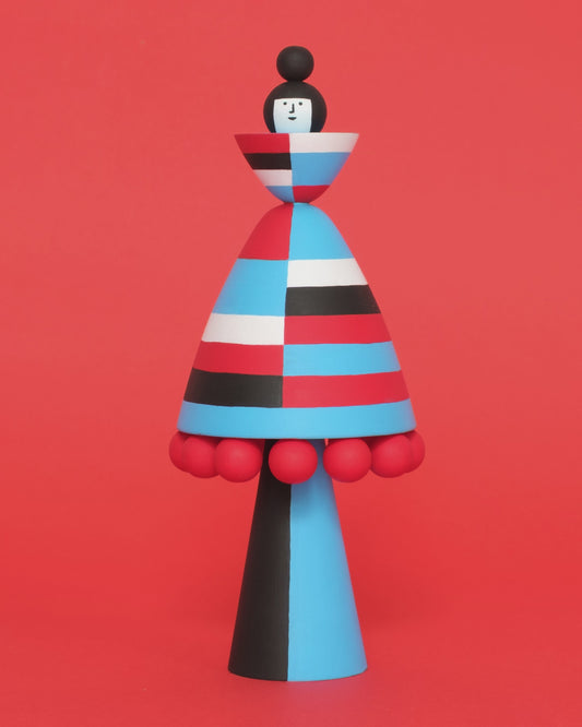A spinning wooden figure with red, blue, black and white stripes on a plain orange background.