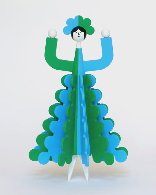 A spinning video of a colourful wooden sculpture with a green and blue stripey 3D skirt and a matching headdress with white legs on a plain white background.