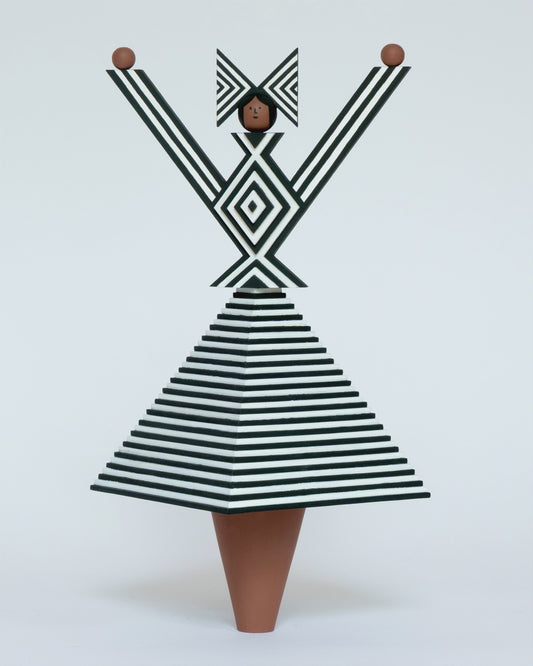 A spinning video of a monochrome wooden sculpture with a black and white stripey 3D top and skirt and a matching headdress with brown legs on a plain white background.